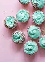 Cupcakes adorned with blue frosting and sprinkles, set against a charming pink backdrop.
