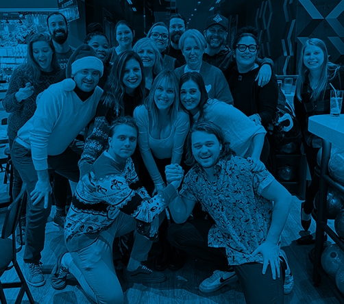 A smiling group of UPBrand employees in a bowling alley wearing Ugly Holiday Sweaters and hats.