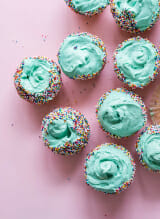 Cupcakes adorned with blue frosting and sprinkles, set against a charming pink backdrop.