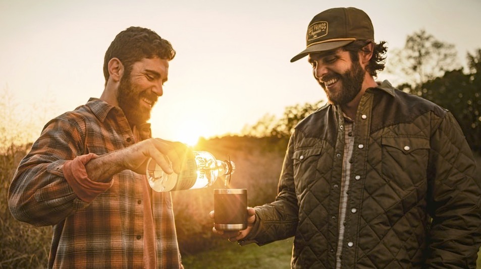 Two men outside pouring Dos Primos Tequila into a glass