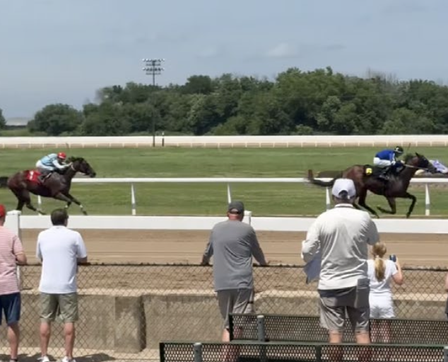 Spectators at the rail watch two jockeys race horses down the track