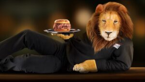The Lion's Choice lion reclining in a black tracksuit, offering a roast beef sandwich on one paw.