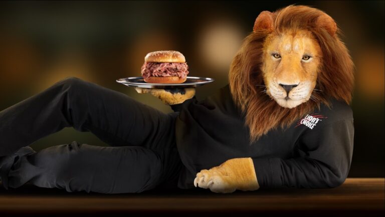 The Lion's Choice lion reclining in a black tracksuit, offering a roast beef sandwich on one paw.