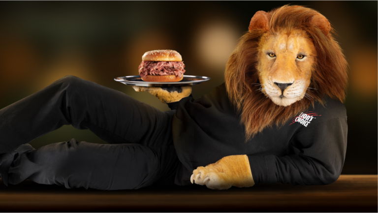 The Lion's Choice lion reclining in a black tracksuit, offering a roast beef sandwich on one paw.